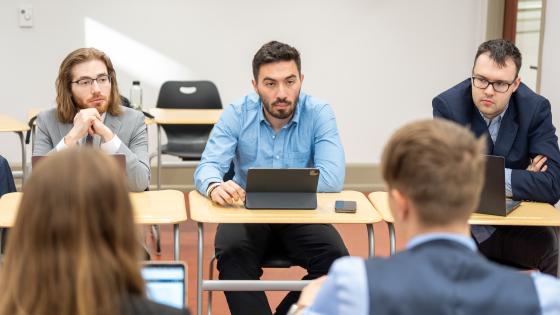 Five students negotiate in an ISCNE. Three facing the camera and two facing away seated in desks.